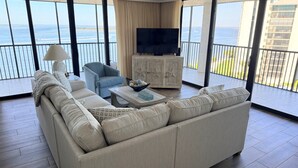 Ein geräumiges Wohnzimmer mit einem großen Sofa, einem Fernseher und Blick auf den Ozean.