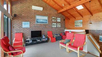 A spacious living area with a brick wall, wooden ceiling, and a flat-screen TV.