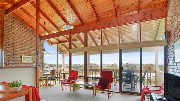 Una habitación amplia con techo alto, ventanas grandes y un balcón con mobiliario exterior.