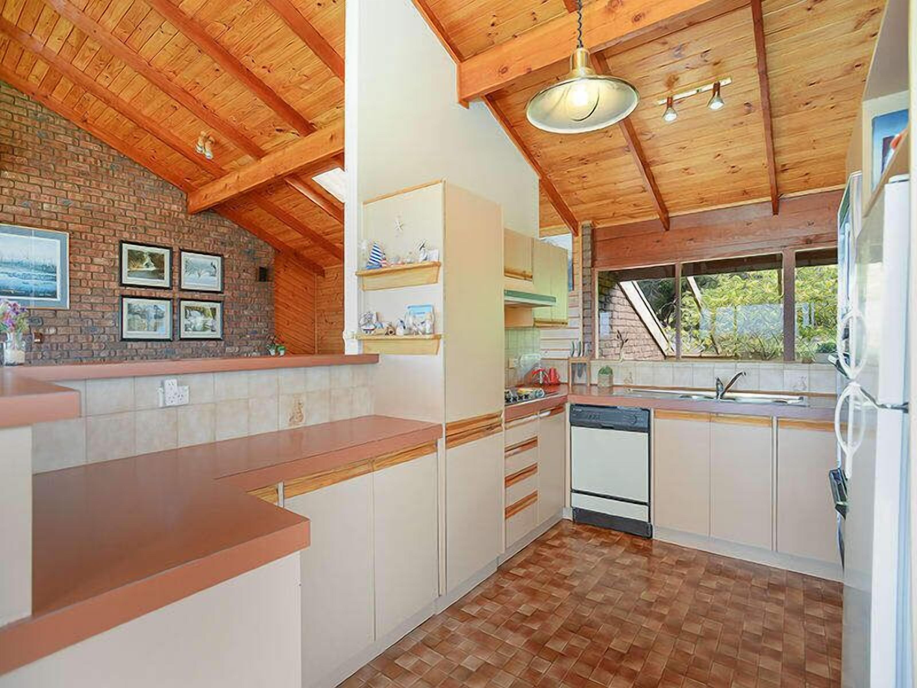 A kitchen with wooden beams, a brick wall, and a window with a view.