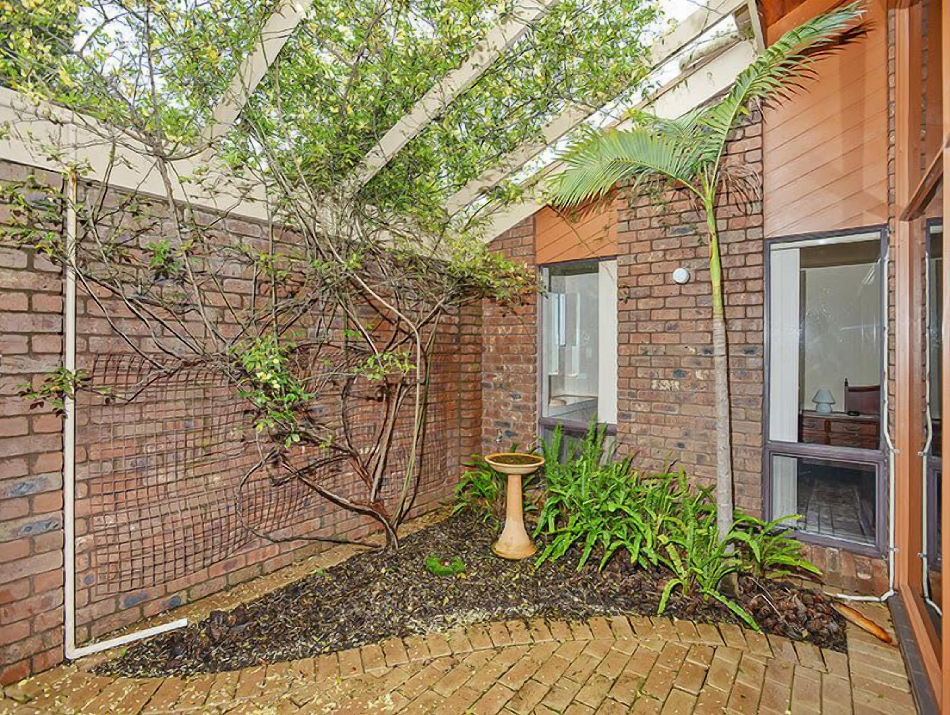 A brick building with a window, a door, and a small garden area with plants and a birdbath.