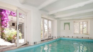 Une piscine à l’eau claire, entourée de murs blancs et dotée d’un balcon orné de fleurs violettes.