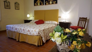 Un dormitorio con cama, mesita de noche, lámpara, silla y un jarrón con flores.
