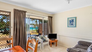Ein Zimmer mit Fernseher, Korbmöbeln, einer Couch und Blick auf den Strand.