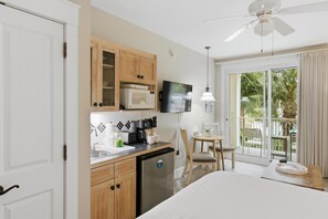 Une chambre d’hôtel compacte comprenant un coin cuisine, un lit, un espace repas et un balcon avec vue sur les palmiers.