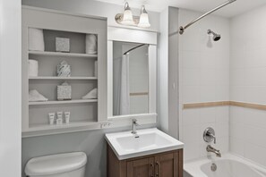 Une salle de bain avec un lavabo blanc, un miroir, une douche et des étagères contenant des articles de toilette.