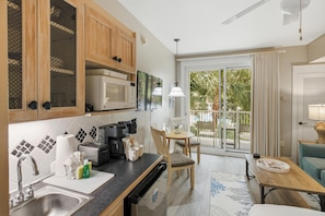A kitchen with a sink, stove, and microwave, a dining area with a table and chairs, and a sliding glass door to a balcony.