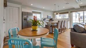 A modern kitchen with white cabinets, a stainless steel refrigerator, and a dining area with a round wooden table and blue chairs. - Seaglass Shores: New 2BR/2BTH Modern Condo With Bay & Ocean Views (San Diego)