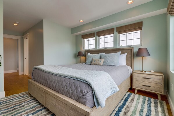 A bedroom with a large bed, two bedside tables, and a window with blinds.
