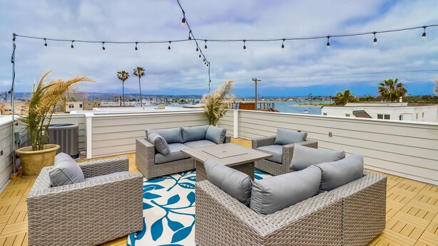 A rooftop patio with wicker furniture, string lights, and a view of the city. - Seaglass Shores: New 2BR/2BTH Modern Condo With Bay & Ocean Views (San Diego)