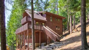 Eine Holzhütte mit Balkon und Treppe, umgeben von Bäumen.