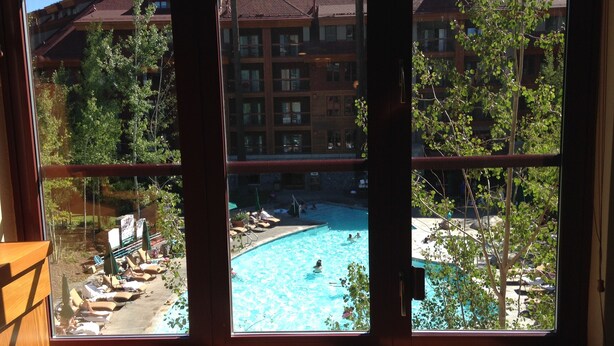 A view of a swimming pool with people in the water, surrounded by trees and a building with multiple balconies.