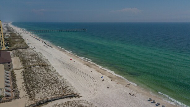 Luchtbeeld van een strand met een pier die in de oceaan uitsteekt, een zandstrand en een gebouw met een balkon met uitzicht op het strand.