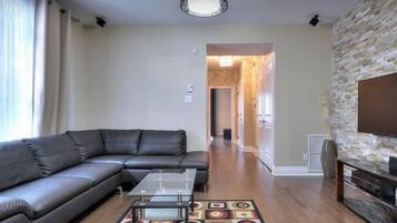 Una sala de estar con un sofá modular, una mesa de centro, un tapete estampado, una pared de piedra decorativa y un televisor.