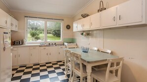 A kitchen with white cabinets, a checkered floor, a window with a view of greenery, and a table with chairs. - Aireys Inlet Cottage (Aireys Inlet)