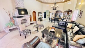 Un salón espacioso con chimenea, sofá de cuero, sillas con estampado de cebra y un comedor con candelabro.