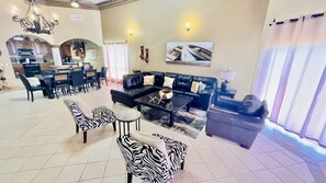 A spacious living area with a sofa set, a coffee table, and zebra-patterned chairs. A dining area with a table and chairs is visible in the background.