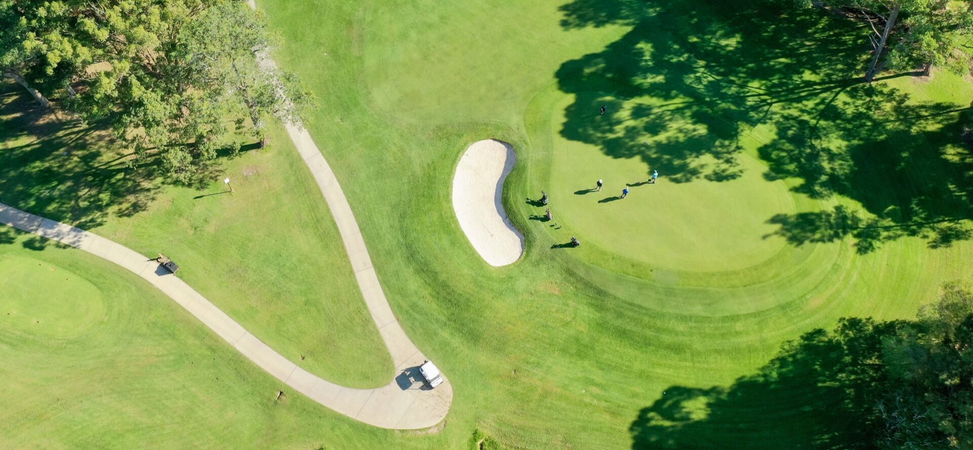 An aerial view of a golf course with a sand bunker, a tee box, and a putting green.