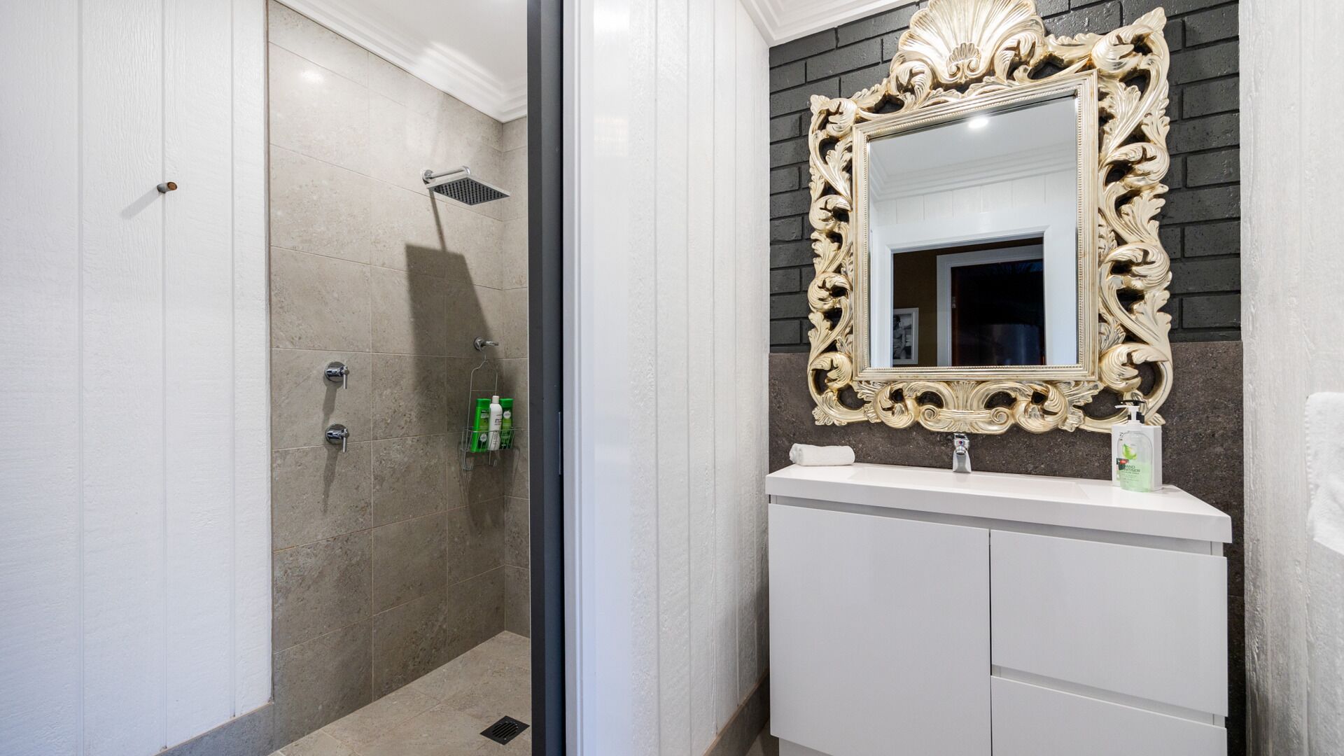 Une salle de bain équipée d’une douche, d’un meuble-lavabo et d’un grand miroir décoratif.