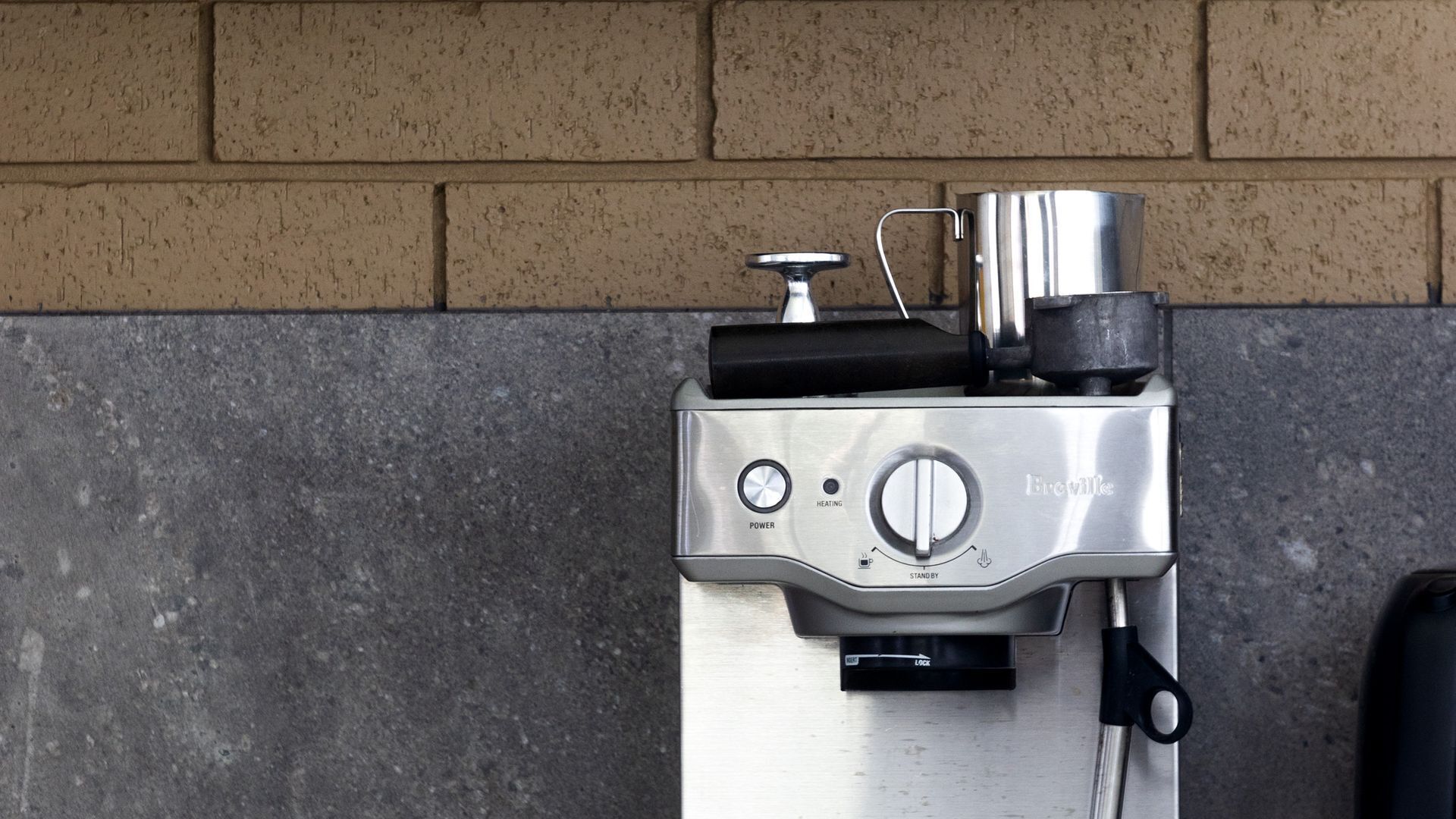 A Breville espresso machine mounted on a wall with a brick pattern background.
