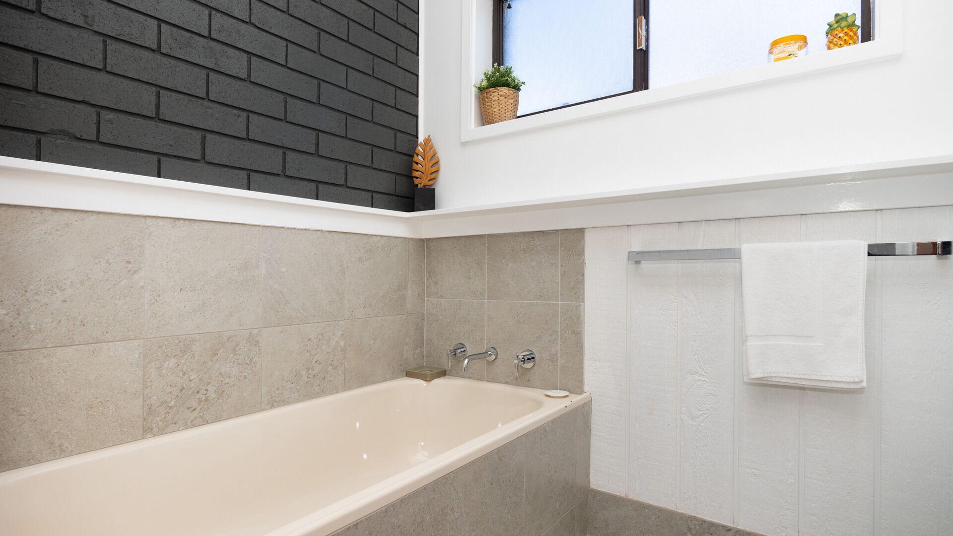 A modern bathroom with a bathtub, a window with a view of the sky, and a small plant on the windowsill.