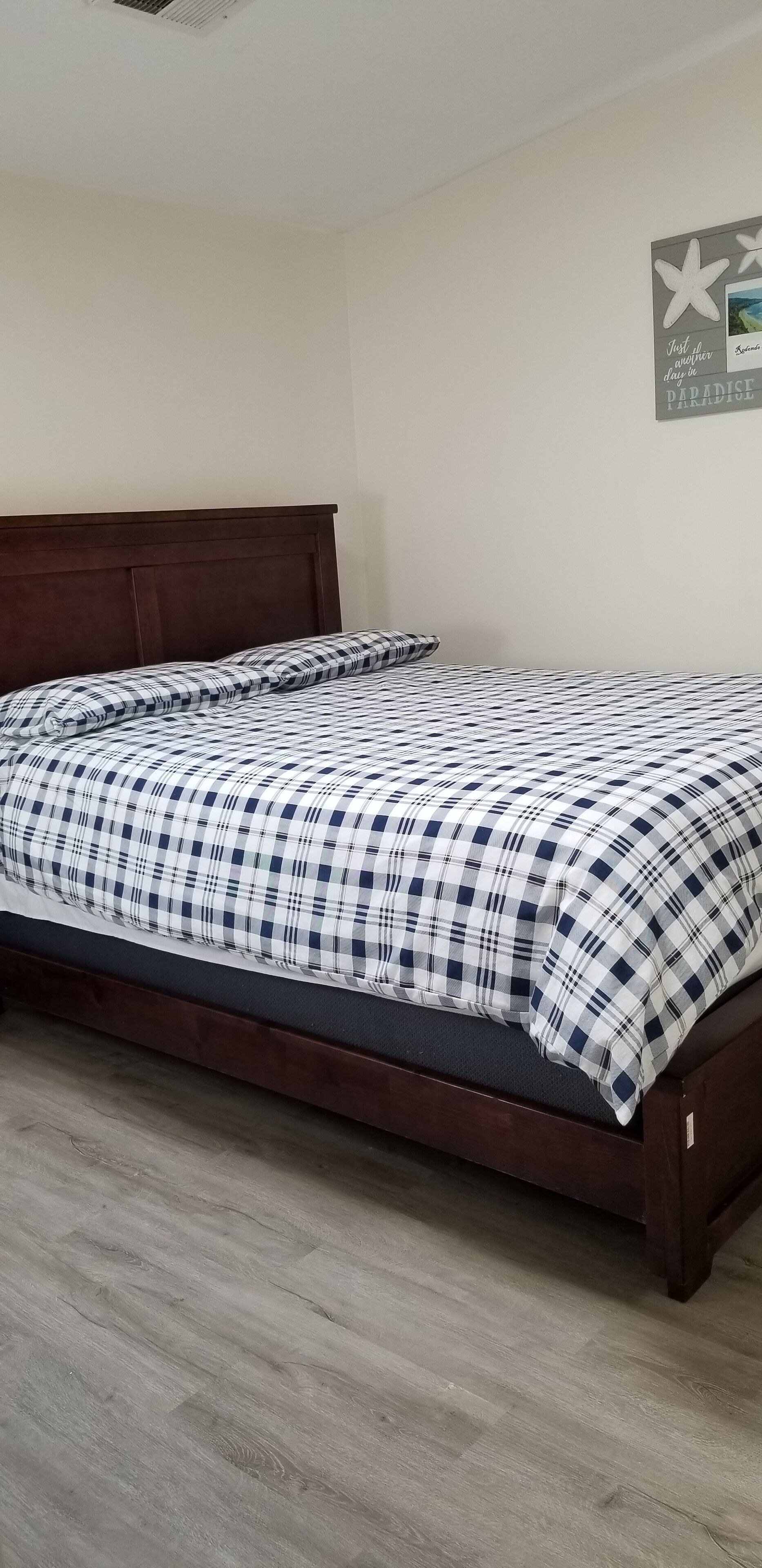 A single bed with a dark wooden headboard, a checkered bedspread, and a wall with a starfish decoration and a motivational quote.