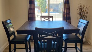 Un coin repas comprenant une table rectangulaire et quatre chaises, une fenêtre avec des rideaux et une vue sur l’extérieur.