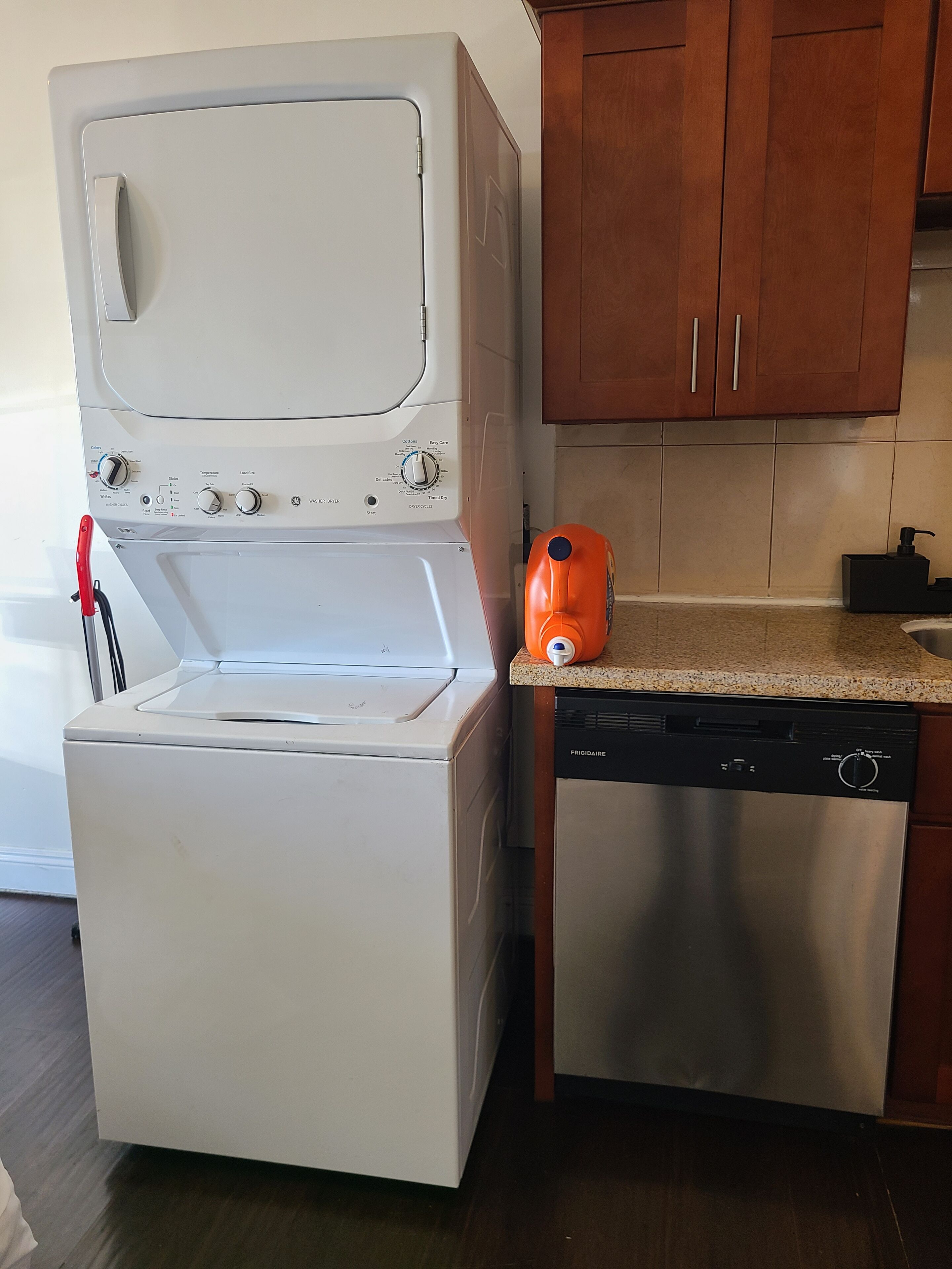 A compact kitchen with a white washing machine, a stainless steel dishwasher, and wooden cabinets.