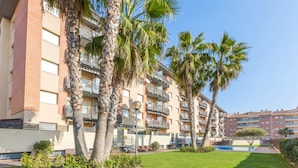 A multi-story residential building with balconies, a swimming pool, and palm trees.