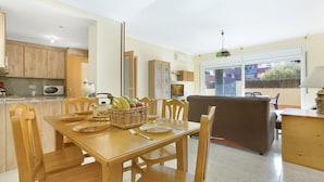 A modern kitchen with wooden cabinets, a dining table set with chairs, a TV, and a balcony with a view.