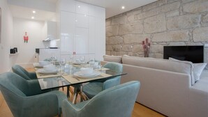 Ein modernes Wohnzimmer mit Steinwand, einem Glastisch, türkisfarbenen Sesseln und einem weißen Sofa.