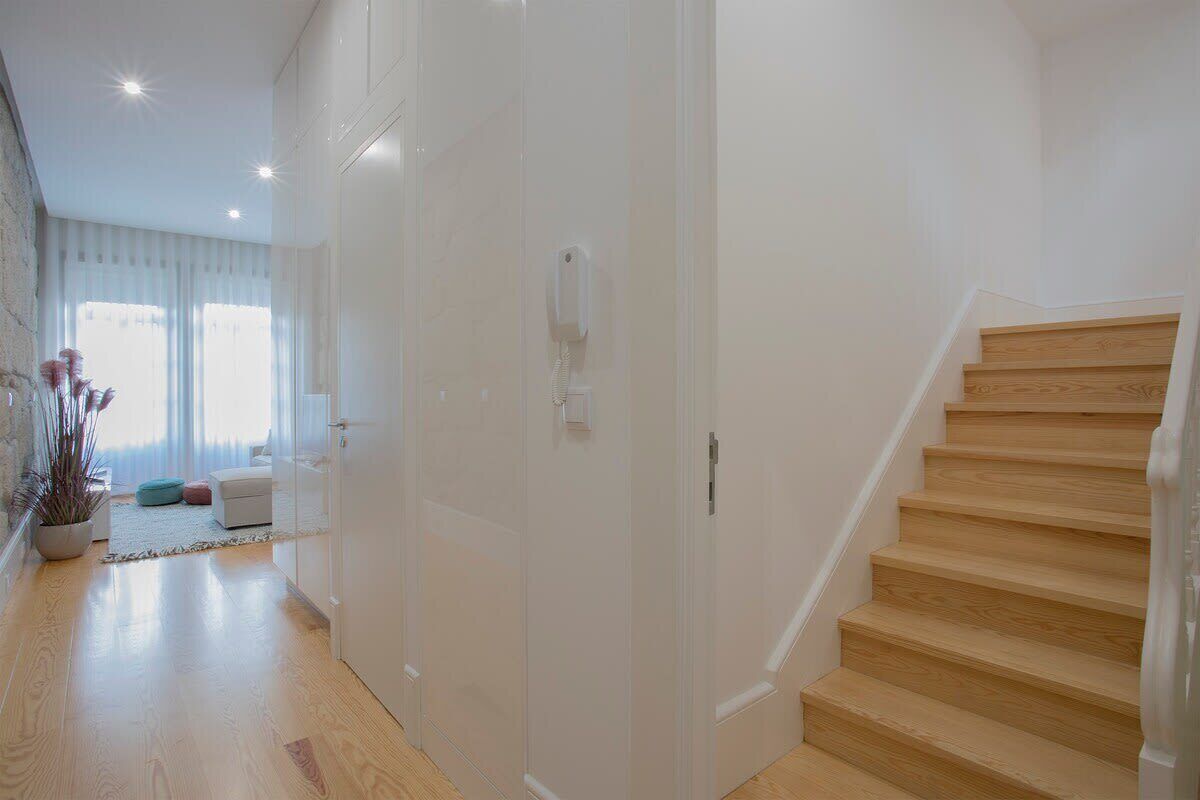 A modern interior with a wooden staircase, a white door, and a living area with a sofa and a plant.