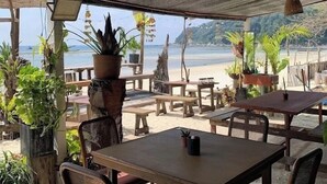 An outdoor seating area with tables and chairs, surrounded by potted plants, overlooking a beach. - Perhentian Cabana (Pulau Perhentian Besar)