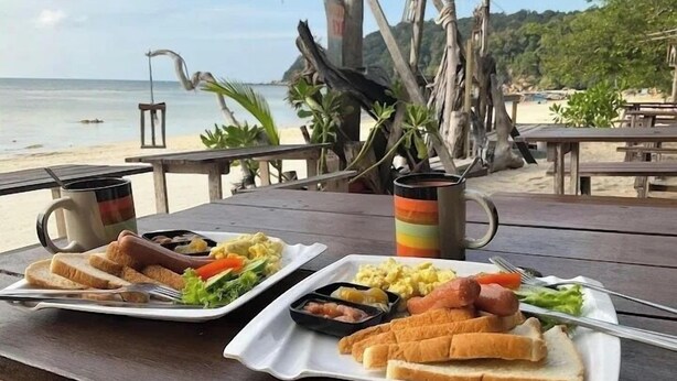 A beachside dining table with plates of food, a mug, and a view of the ocean. - Perhentian Cabana (Pulau Perhentian Besar)
