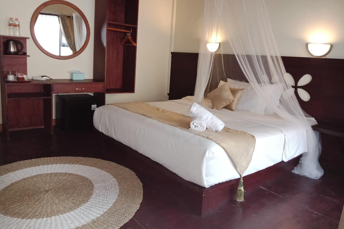 A neatly arranged hotel room with a bed, bedside table, mirror, wardrobe, and a round rug.