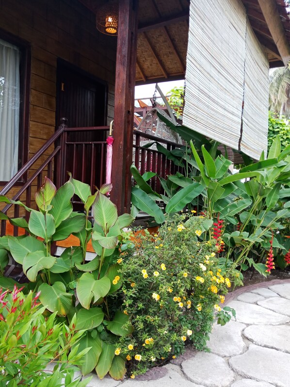 A wooden porch with a railing, surrounded by various plants and flowers.