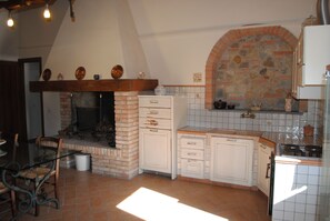 A kitchen with a brick fireplace, white cabinets, and a tiled backsplash. - Farmhouse in Tuscan countryside next to Florence city center. (Firenze)