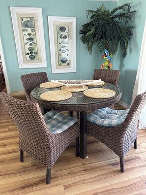 A round glass table with woven placemats, surrounded by wicker chairs with checkered cushions.
