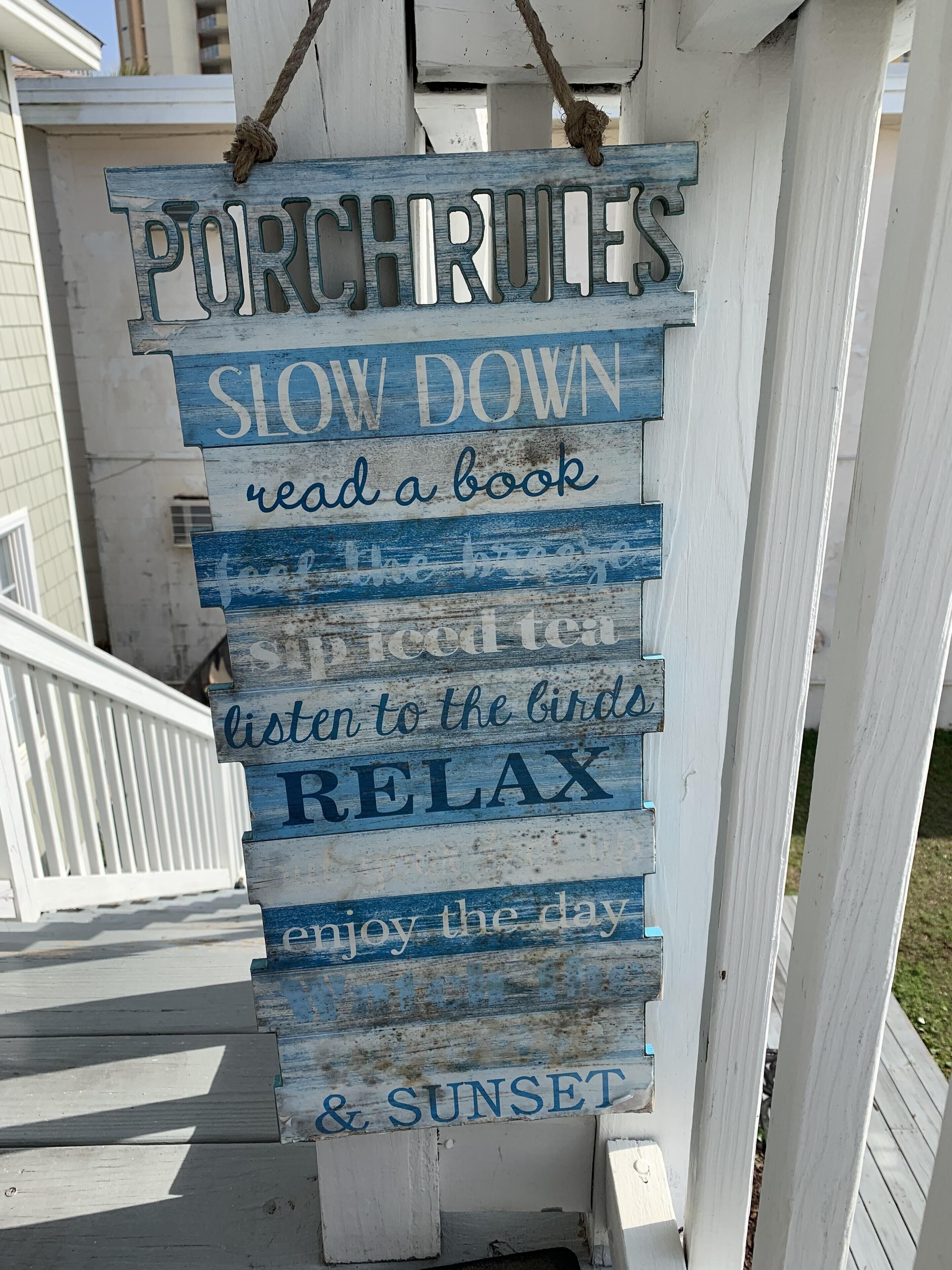 Ein Holzschild mit der Aufschrift 'PORCH RULES' und 'Langsam machen, ein Buch lesen, den Vögeln lauschen, entspannen, den Tag genießen & Sonnenuntergang.'