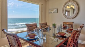 A dining area with a view of the ocean, a round mirror, and a table set with glassware and plates.