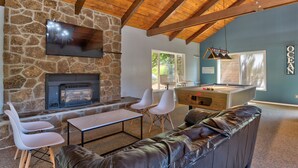 A cozy living area with a stone fireplace, a pool table, and a leather sofa.
