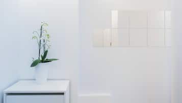 A white room with a potted orchid on a white table and a wall-mounted mirror.