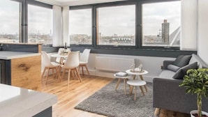 A modern apartment with large windows, a dining area, a sofa, and a plant. - 26 Penge House (London)