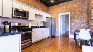 Una cocina con armarios blancos, electrodomésticos de acero inoxidable y una pared de ladrillo.