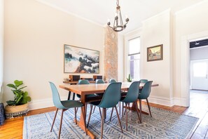 A dining area with a wooden table, six chairs, a chandelier, and artwork on the walls.