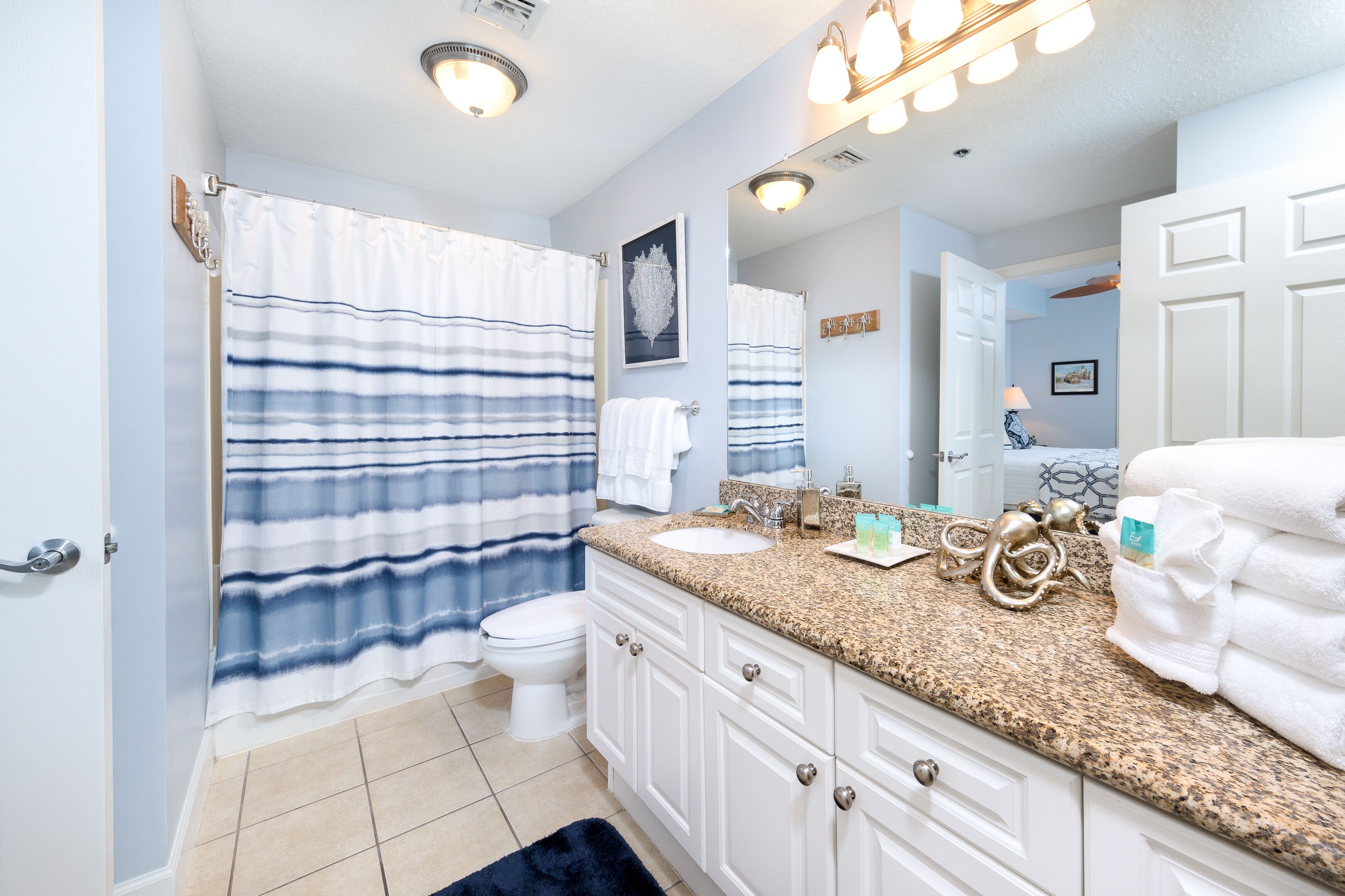 A bathroom with a white toilet, a sink, and a vanity with a mirror. There are towels and toiletries on the counter.