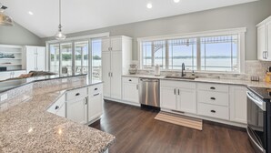 A modern kitchen with white cabinets, granite countertops, and a view of the water. - Crystal Lakefront Luxury Condo – North Shore, Crystal, Michigan (Crystal)