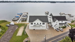 A large white house with a garage, a driveway, and a dock with boats. - Crystal Lakefront Luxury Condo – North Shore, Crystal, Michigan (Crystal)