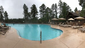 A swimming pool with lounge chairs and umbrellas, surrounded by tall trees and a building with a wooden roof. - Torreon 3 BR home - Golf membership available (Show Low)