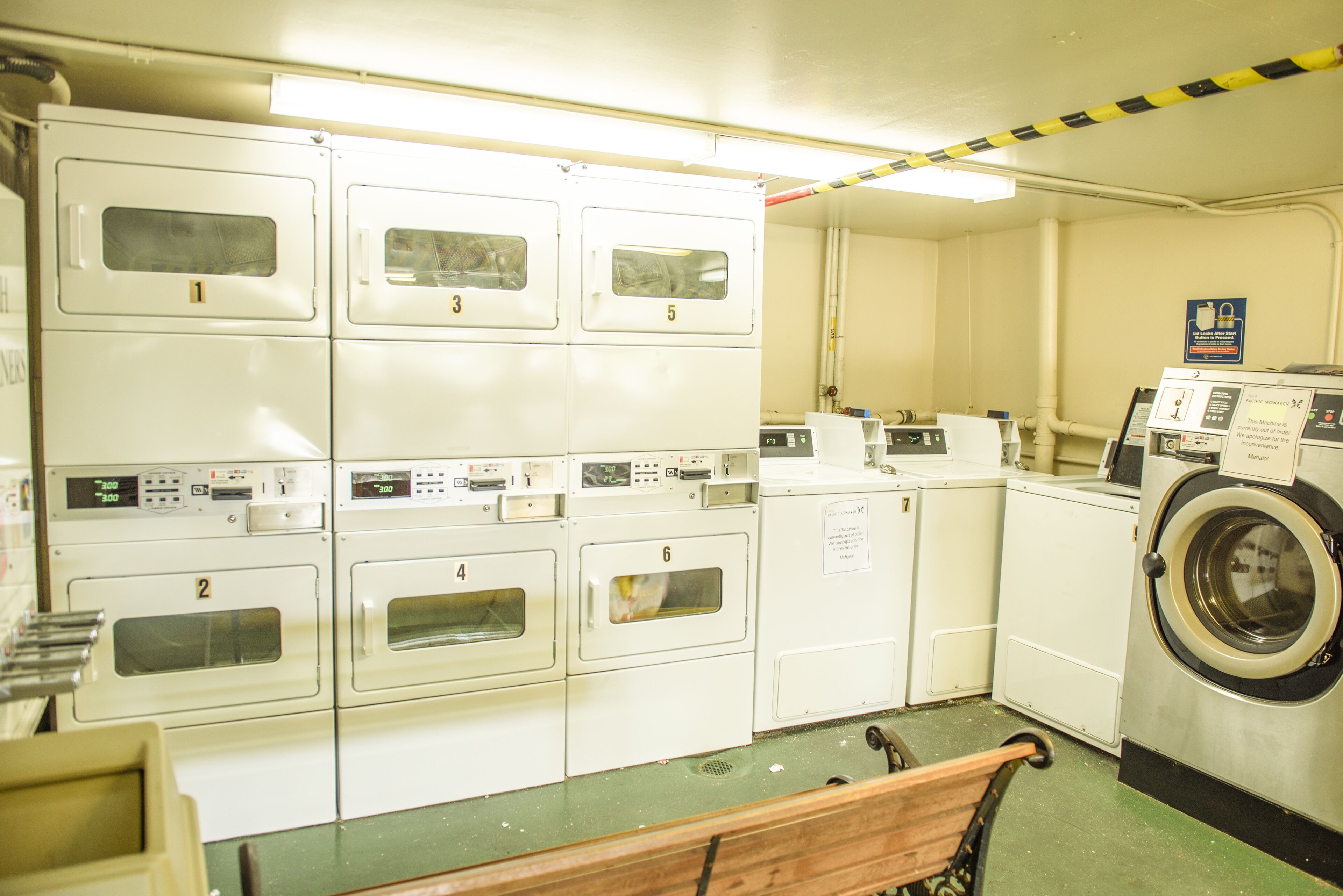 Une buanderie équipée de plusieurs machines à laver et de plusieurs sèche-linge, numérotés de 1 à 6, et un banc situé au premier plan.